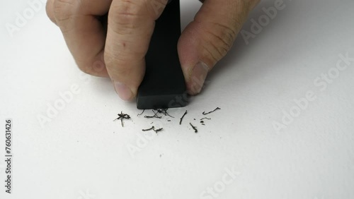 Hand holding black eraser scrap on paper background. 
Error Eraser dust delete wrong words on white background.
top view.   Slow motion.