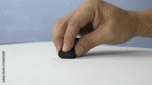 Hand holding black eraser scrap on paper background. 
Error Eraser dust delete wrong words on white background.
top view.   Slow motion.