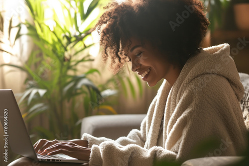 Woman in a robe sitting on a couch with a laptop in front of her, working from home tranquilly