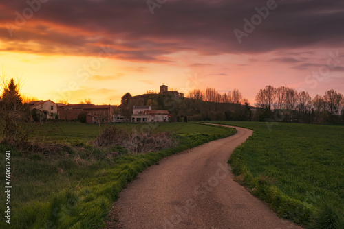 Colorful and warm sunset in Buenavista de Valdavia, Palencia, on a winding road between green cereal fields with the church on top of a hill photo