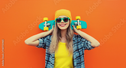 Summer portrait of happy cheerful stylish young woman with skateboard posing on orange background