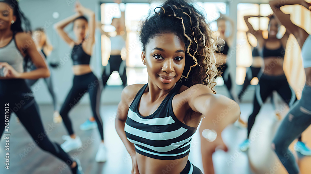 A young woman with curly hair is dancing in a group of other women. She is wearing a black and white striped sports bra and black leggings.