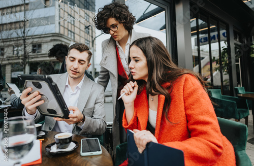 Three businesspeople engage in a discussion over a tablet at an outdoor cafe, with coffee and work essentials on the table. photo