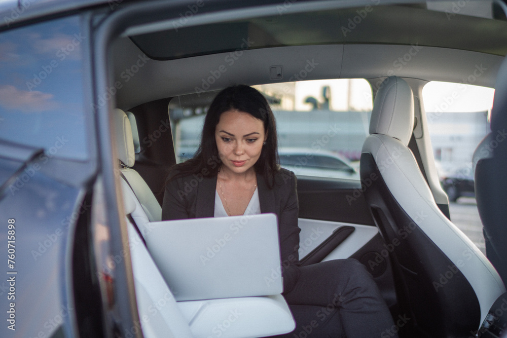 Beautiful businesswoman using laptop while sitting on back seat in the car while working online. Business, people, distance work concept