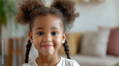 Smiling cute little African American girl with two pony tails looking at camera. Portrait of happy female child at home. Smiling face a of black 4 year old girl looking at camera with afro puff hair. photo