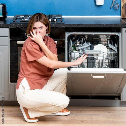 Busy housewife putting dirty plates in dishwasher machine in the kitchen. Household and exhausting cleaning day concept