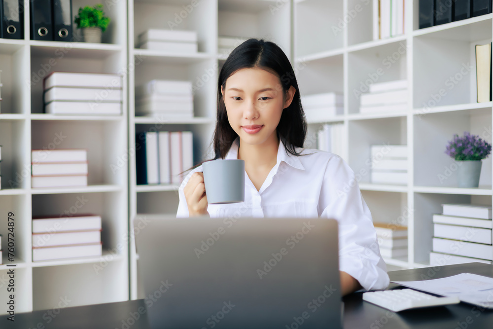 A woman is sitting at a desk with a laptop and a cup of coffee A woman is sitting at a desk with a laptop and a cup of coffee