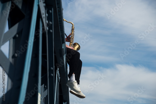 Closeup of musician playing saxophone sitting on a metallic bridge in the street