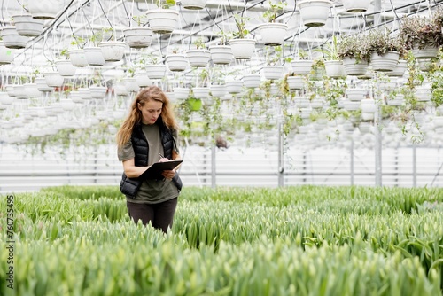 A woman stands in a greenhouse with tulips, watches the growth of flowers and makes notes in a notebook