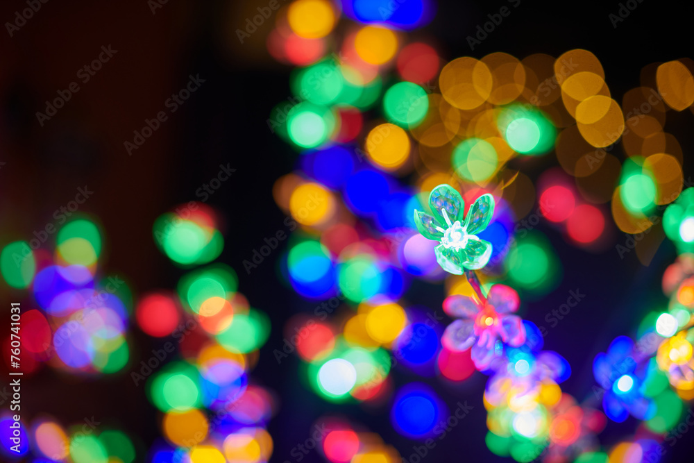 Multicolored garland flower against background of multicolored lights on Christmas night, beautiful New Year lights create atmosphere of wonder and holiday enchantment
