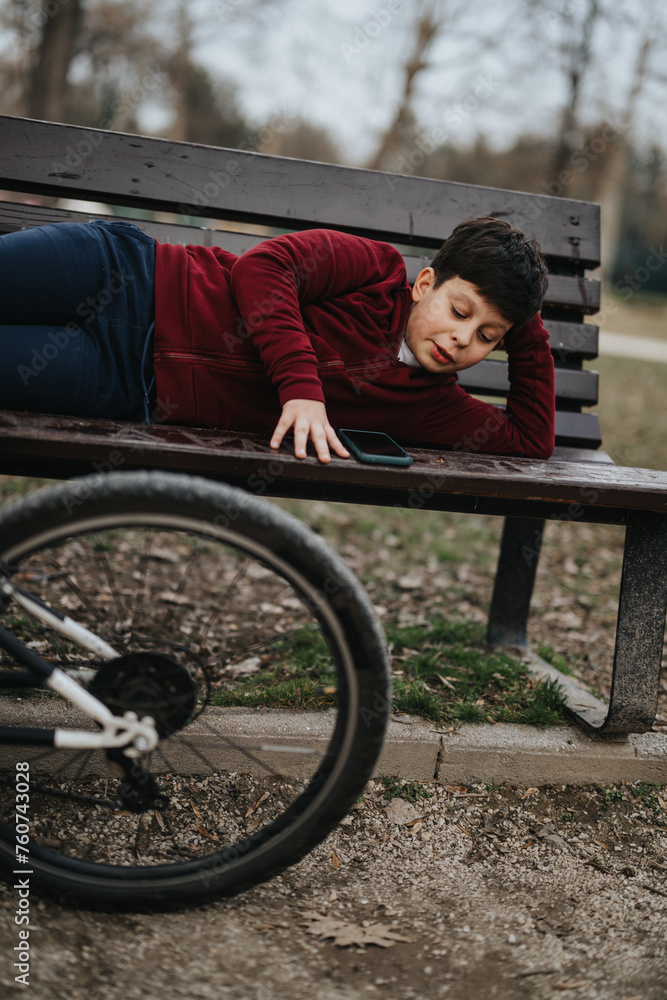 Obraz premium An active young kid enjoys a rest with his bicycle lying nearby in a tranquil park setting.
