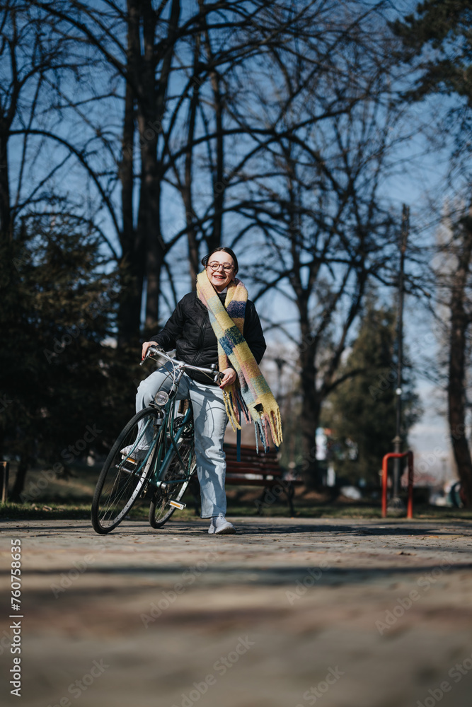 Joyful middle-aged woman wearing glasses and a colorful scarf, standing with her bike in a sunny park setting, exuding positivity and an active lifestyle.