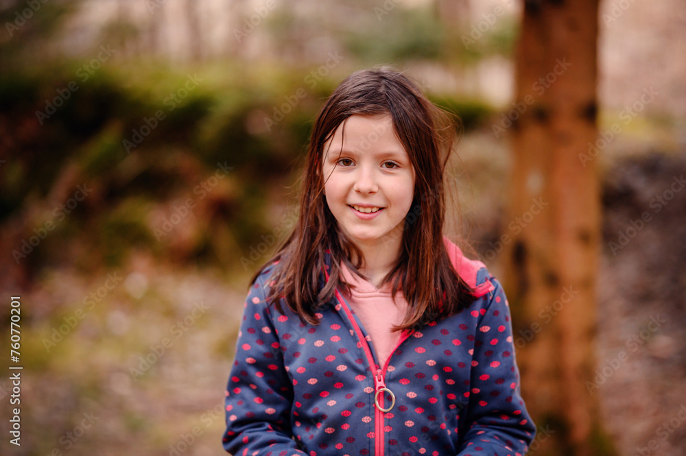 A cheerful young girl with brown hair smiles brightly, wearing a dotted jacket in a lush forest setting, exuding warmth and innocence A cheerful young girl with brown hair smiles brightly, wearing a dotted jacket in a lush forest setting, exuding warmth and innocence