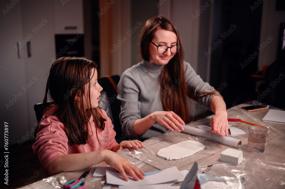 Fototapeta premium A delighted girl with her mother crafting at home, their laughter and enjoyment echoing the warmth of family time and the fun of creating together