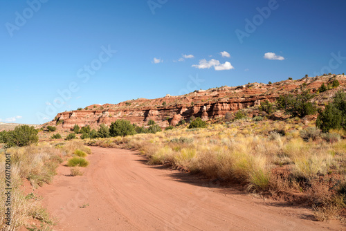 Sandy unpaved road in the desert of Utah with multicolored sandstone formation in the background