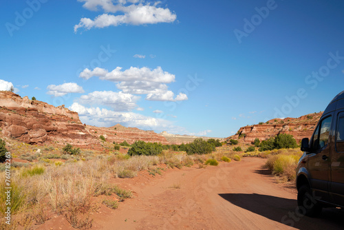 Car driving over the sandy road in the desert of Utah USA with colorful mountains in the background