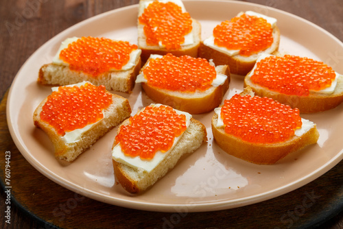 Canapes with red caviar on a plate on a wooden table. Horizontal