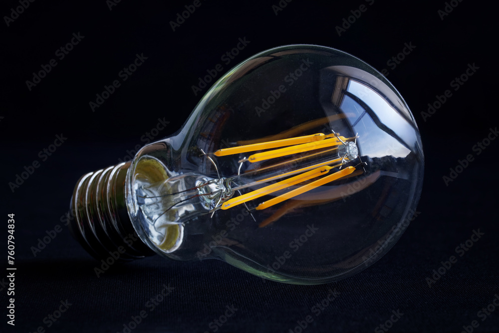 Modern quality transparent LED filament lamp with yellow filaments on a dark background. Saving electricity. Place for inscription. Photo. Copy space Modern quality transparent LED filament lamp with yellow filaments on a dark background. Saving electricity. Place for inscription. Photo. Copy space