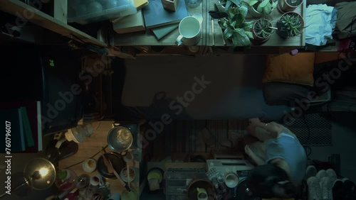 Top time-lapse shot of Chinese girl doing routine activities at home in micro flat in evening - hand-washing clothes, cooking dinner, eating, tidying up, then lying down on bed to watch TV photo