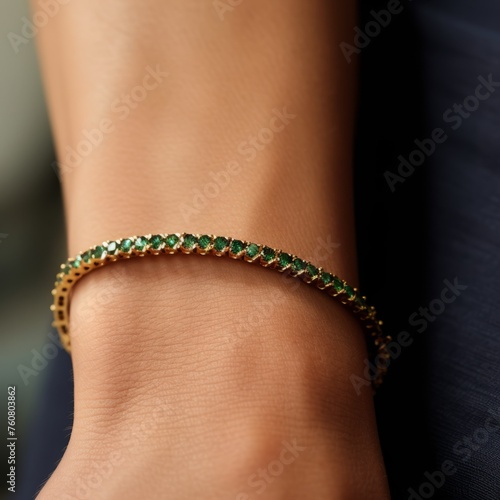 Emerald tennis bracelet with yellow gold on a woman's hand. Closeup image of a beautiful thin gold bracelet with many small emeralds on a soft female hand. Expensive luxury elegant bracelet jewelry.