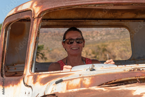 South Africa. 16/02/2024. Attractive woman posing with an old rusty American car on the roadside in the Swartland region of South Africa.