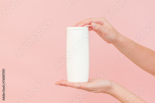 Shampoo, hair conditioner or body lotion bottle in hands in pink background. Cosmetics bottle