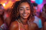 A joyful woman with a beautiful smile and stylish dreadlocks gazes confidently into the camera, exuding warmth and charm in her outdoor setting