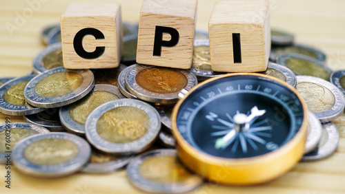 Heap of money coins with CPI word on wooden cubes and gold compass on table background. CPI, or Consumer Price Index, economic data measure that into inflation and the cost of living of consumers.