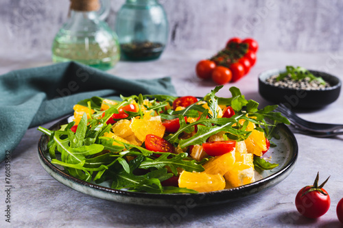 Homemade salad of orange, cherry tomatoes and arugula on a plate on the table