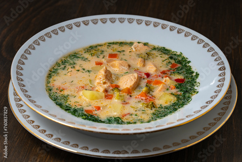 Fresh creamy salmon fish soup with potatoes, carrots, broccoli, peppers and onions in a ceramic plate on a wooden table, closeup. A delicious dinner consists of fish soup with salmon