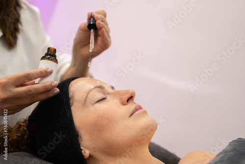 Crop beautician applying serum on client face in beauty salon
