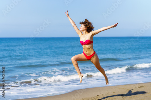 Carefree woman in swimwear jumping on beach