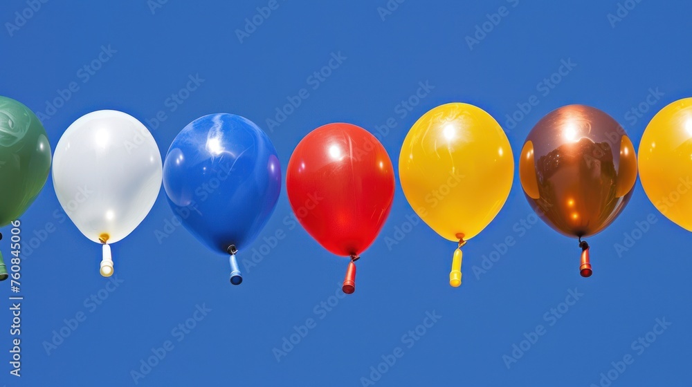a row of multicolored balloons floating in a blue sky with a person in a green shirt looking at them.