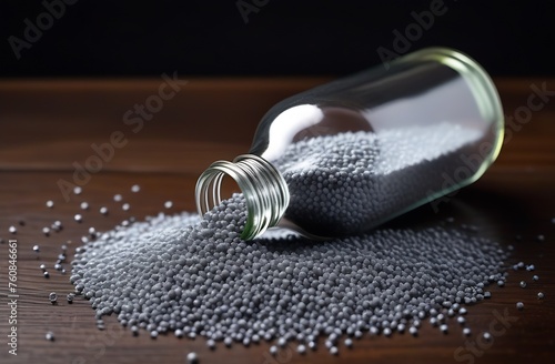 Bottle with gray plastic granules on wooden table photo