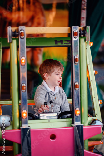 A little boy is absorbed in play, maneuvering a colorful ride with bright lights at a lively fairground