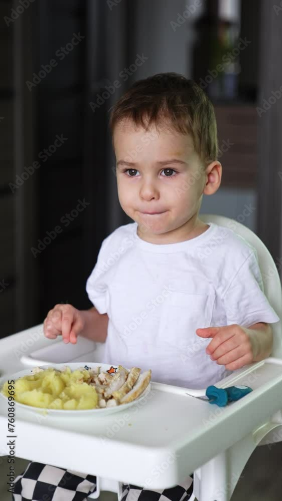 Baby boy sits at high chair with a big plate in front of him. Toddler kid having meals at home. Vertical video. Baby boy sits at high chair with a big plate in front of him. Toddler kid having meals at home. Vertical video.