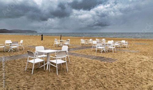 White lounge chairs and table on the sandy beach with stormy sea