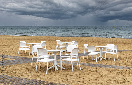 White lounge chairs and table on the sandy beach with stormy sea © konoplizkaya