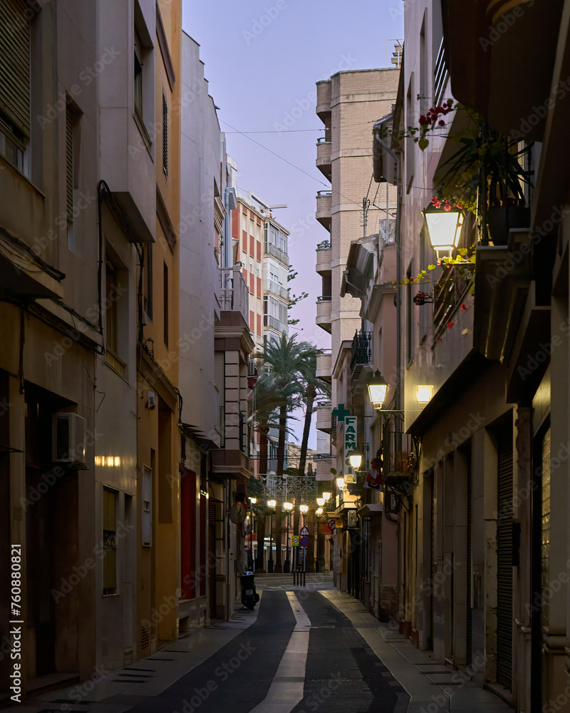 Streets of Cullera. A lively city street scene with tall buildings, palm trees, and diverse architecture. A single streetlight stands out, adding energy and urban flair.