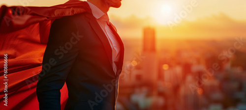 A businessman in a business suit and superhero cape against the backdrop of the city at golden hour © Alina Zavhorodnii