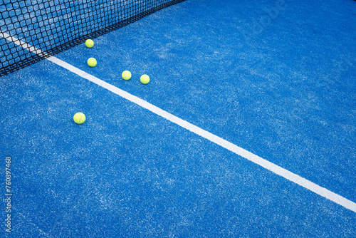 Five balls near the net in a blue paddle tennis court, racket sports concept © Vic