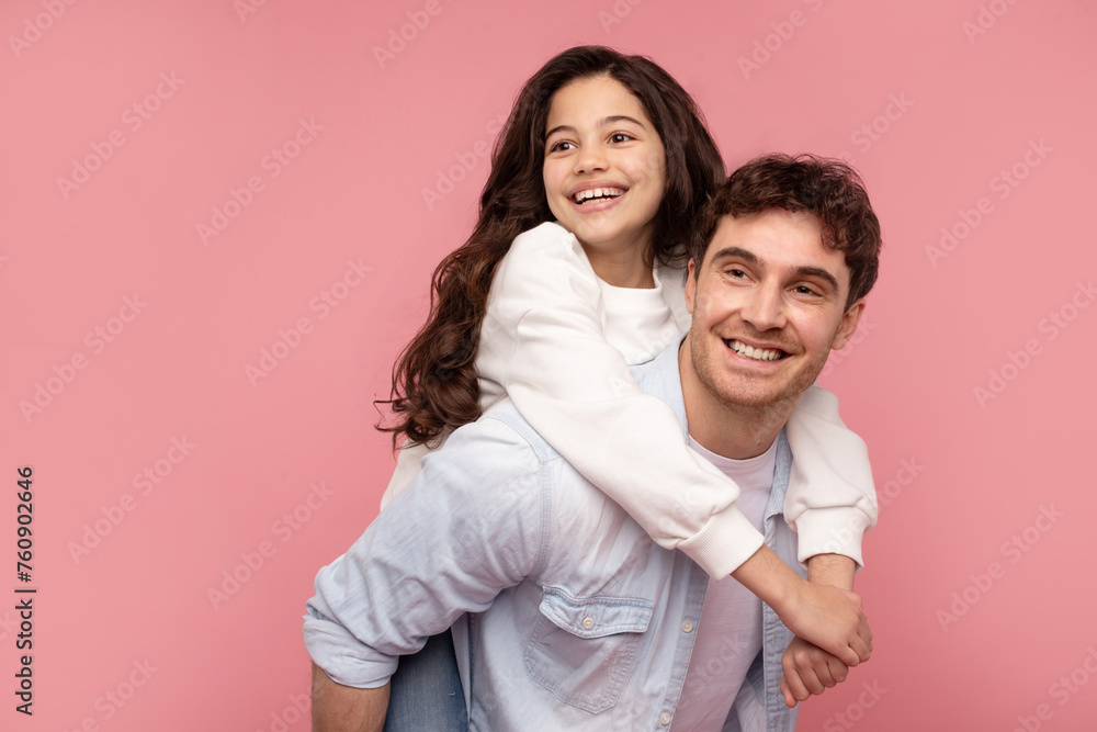 Happy loving daddy carrying daughter on back and both smiling, european family having fun on pink studio background, free space Happy loving daddy carrying daughter on back and both smiling, european family having fun on pink studio background, free space