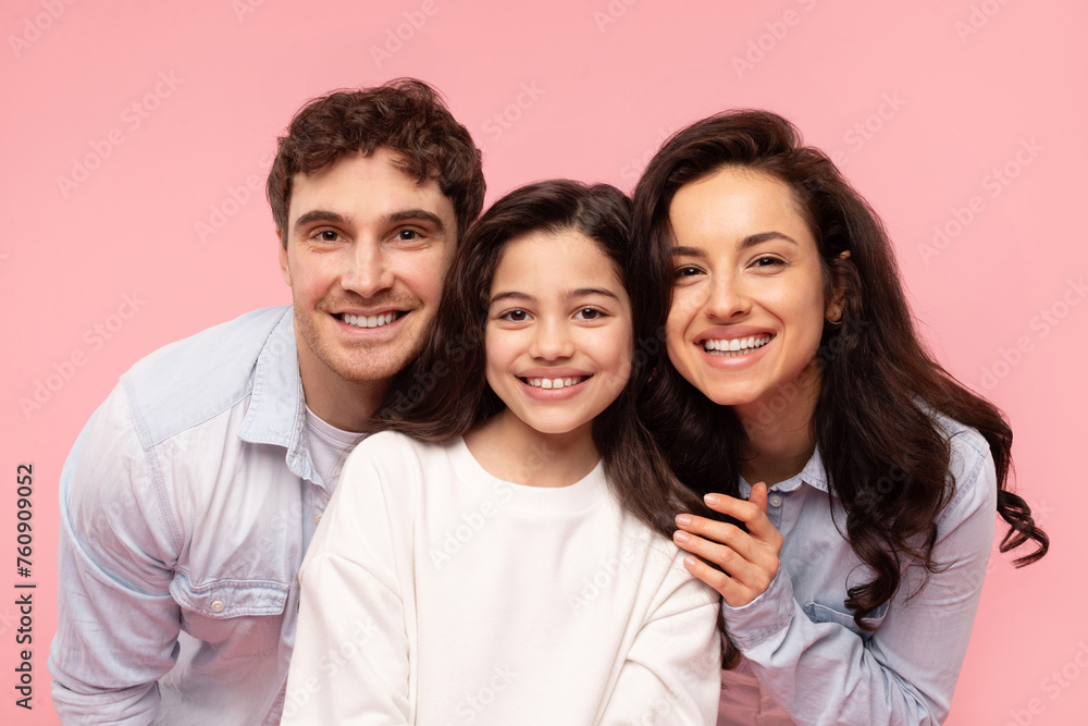 Happy european family of three posing and smiling to camera over pink studio background, mother and father embracing their daughter Happy european family of three posing and smiling to camera over pink studio background, mother and father embracing their daughter