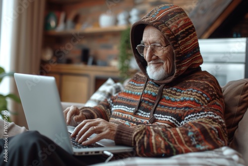 Happiness at work: elderly man in hood on sofa, devotedly doing business at computer photo