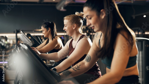 Smiling group of fit young women in sportswear riding on a stationary bikes during a cardio workout session together in a health club photo