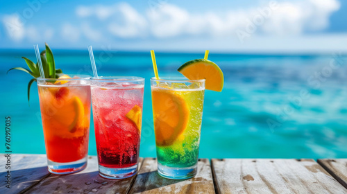 Two drinks with straws in them are on a table by the ocean. The drinks are orange and pink, and they are garnished with slices of lime. The scene is relaxing and inviting