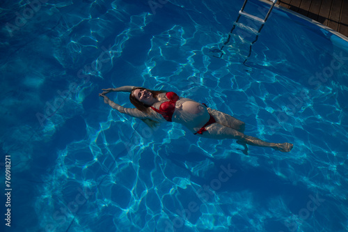 Top view of pregnant woman floating in pool in red bikini. 
