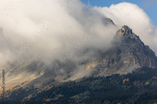 A mountain covered in clouds with a few trees in the foreground