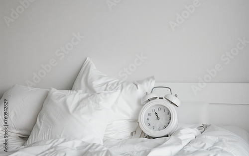 White alarm clock next to white pillows on a white background, good sleep early wake-up call