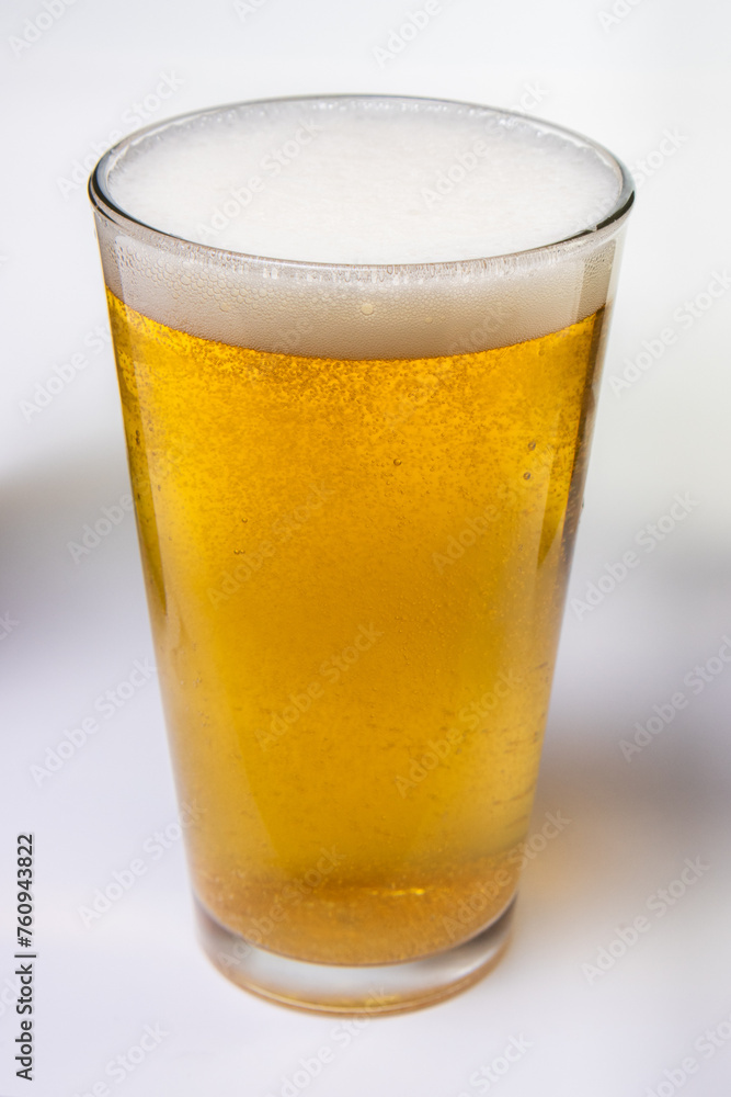 A glass of beer is full and has foam on top A glass of beer is full and has foam on top